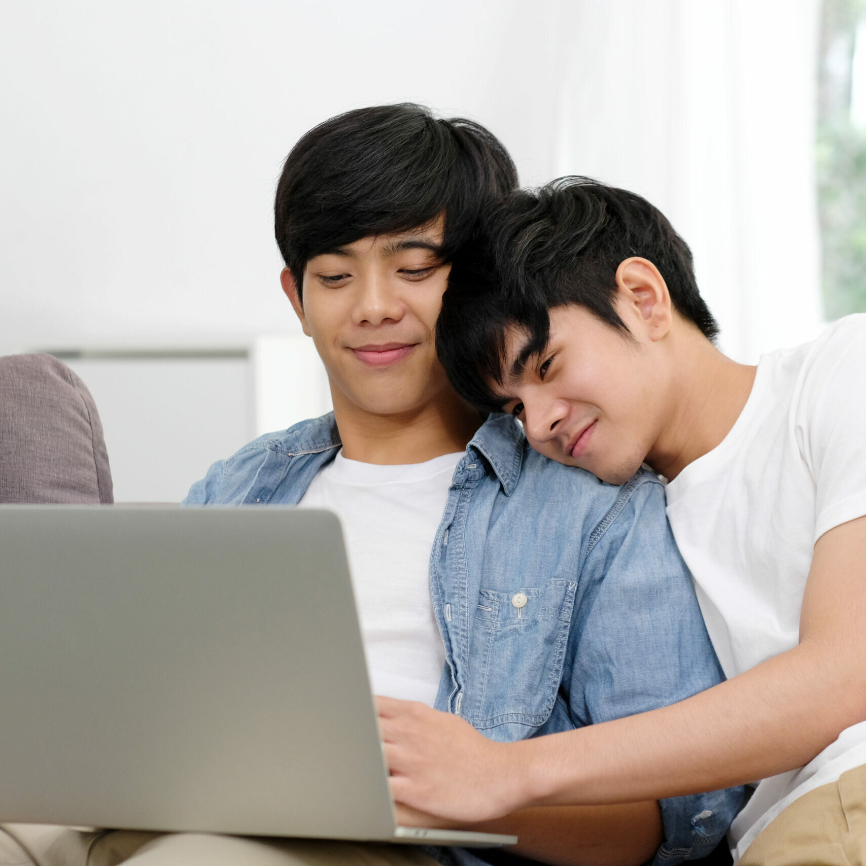 appy young asian homosexual couple in casual clothes using laptop computer while sitting onsofa at home