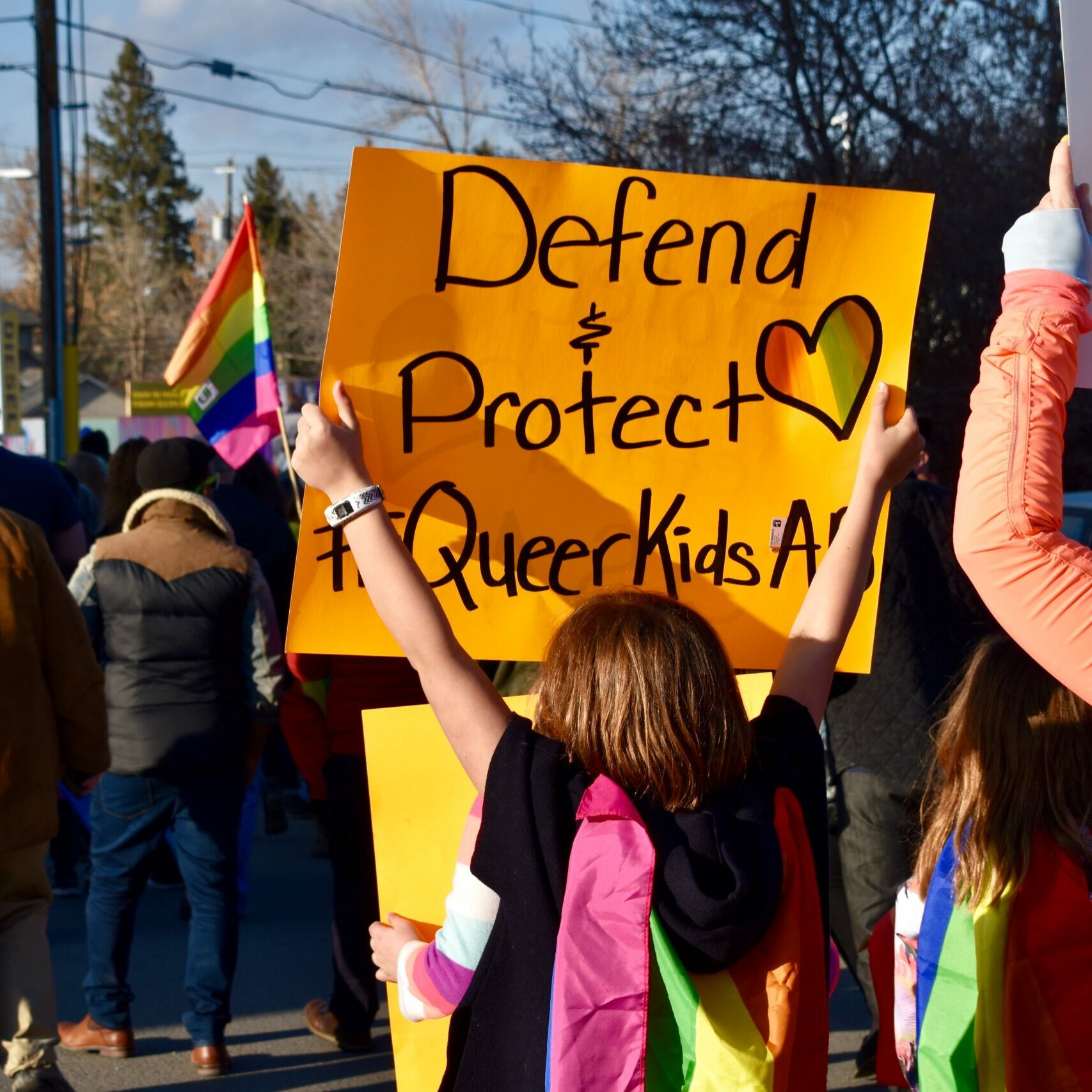 Image of people at a protest. One child holds up a sign that says Defend and Protect Queer Kids