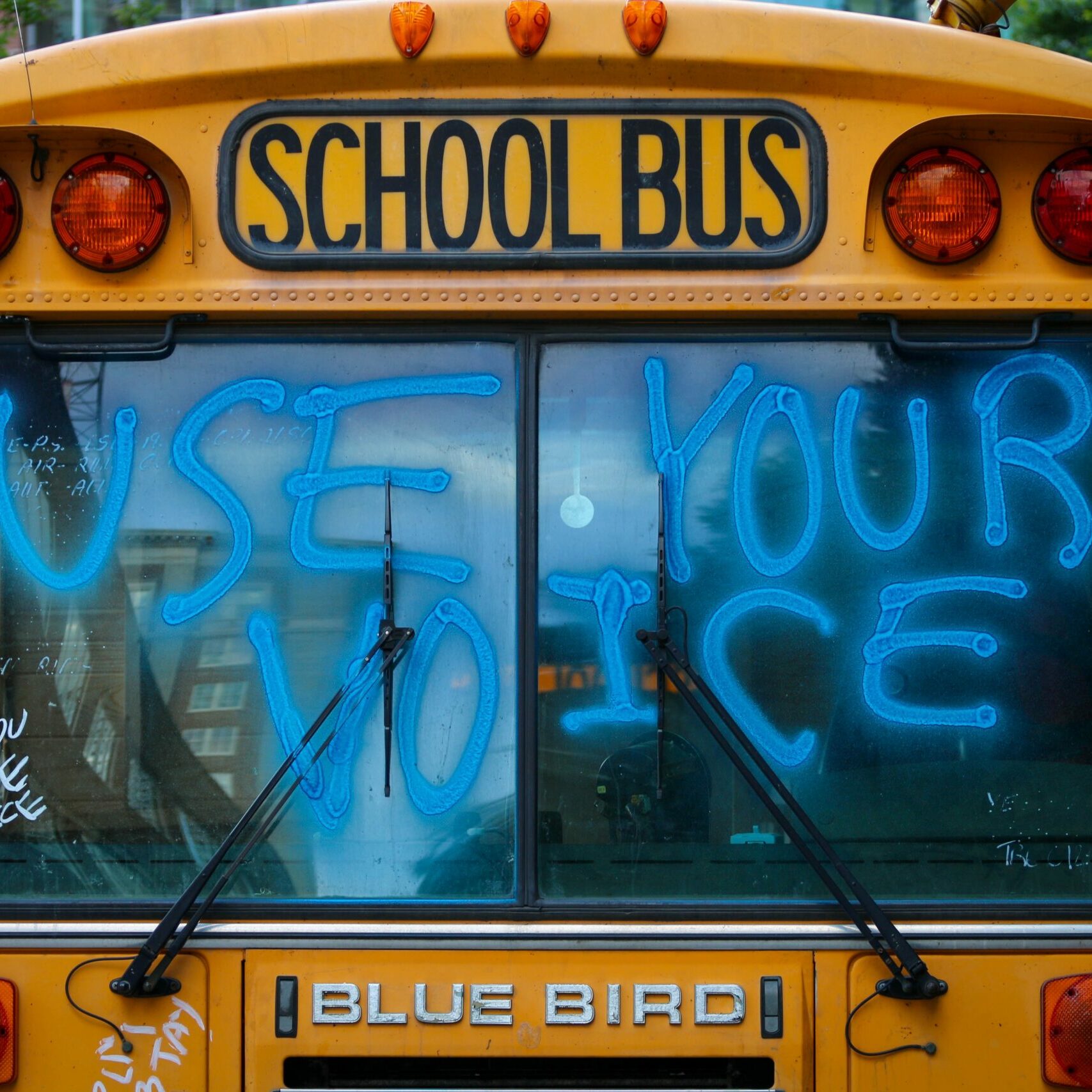 Image of the front of a school bus with the front windshield saying "use your voice" spray painted in blue